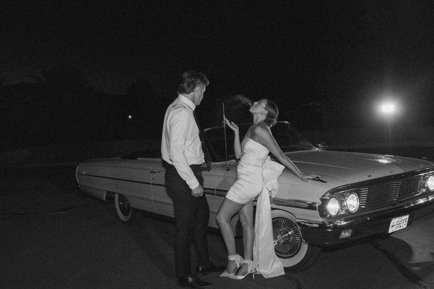 Couple leaning on a vintage car at night, black and white