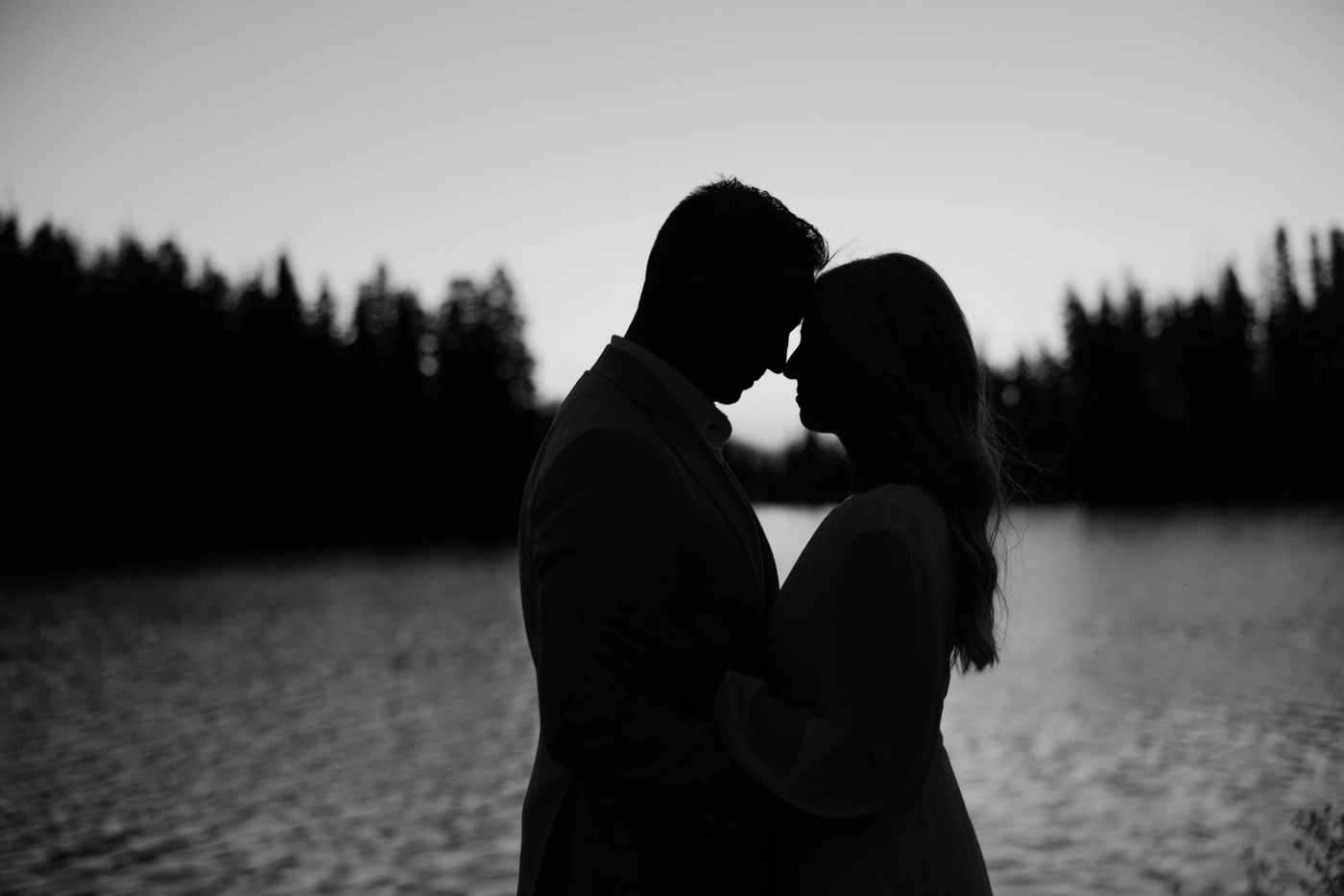 Couple forehead to forehead in silhouette by the lake