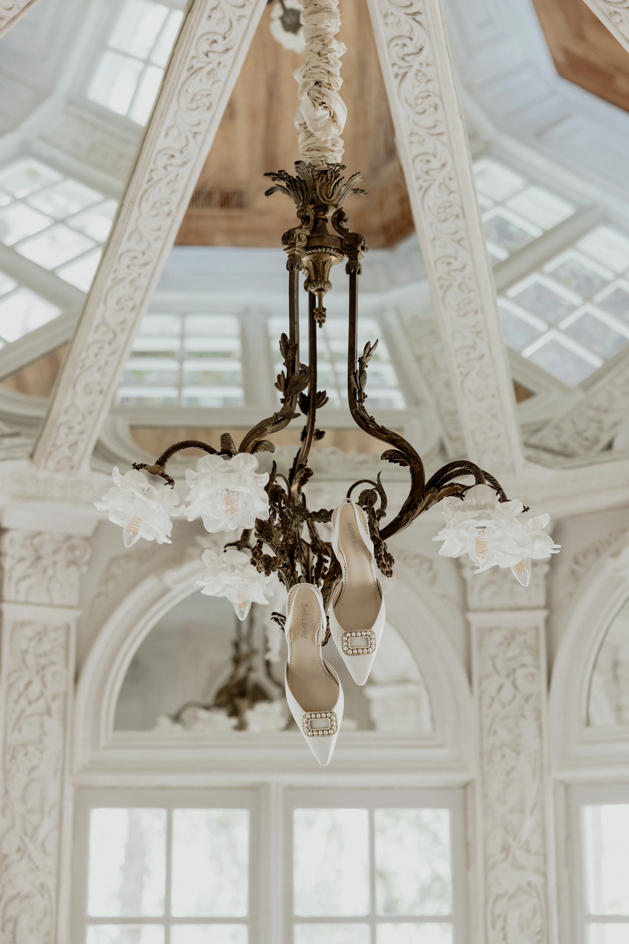 Tasia's pearl-buckle wedding heels hanging from a chandelier in the conservatory at La Caille