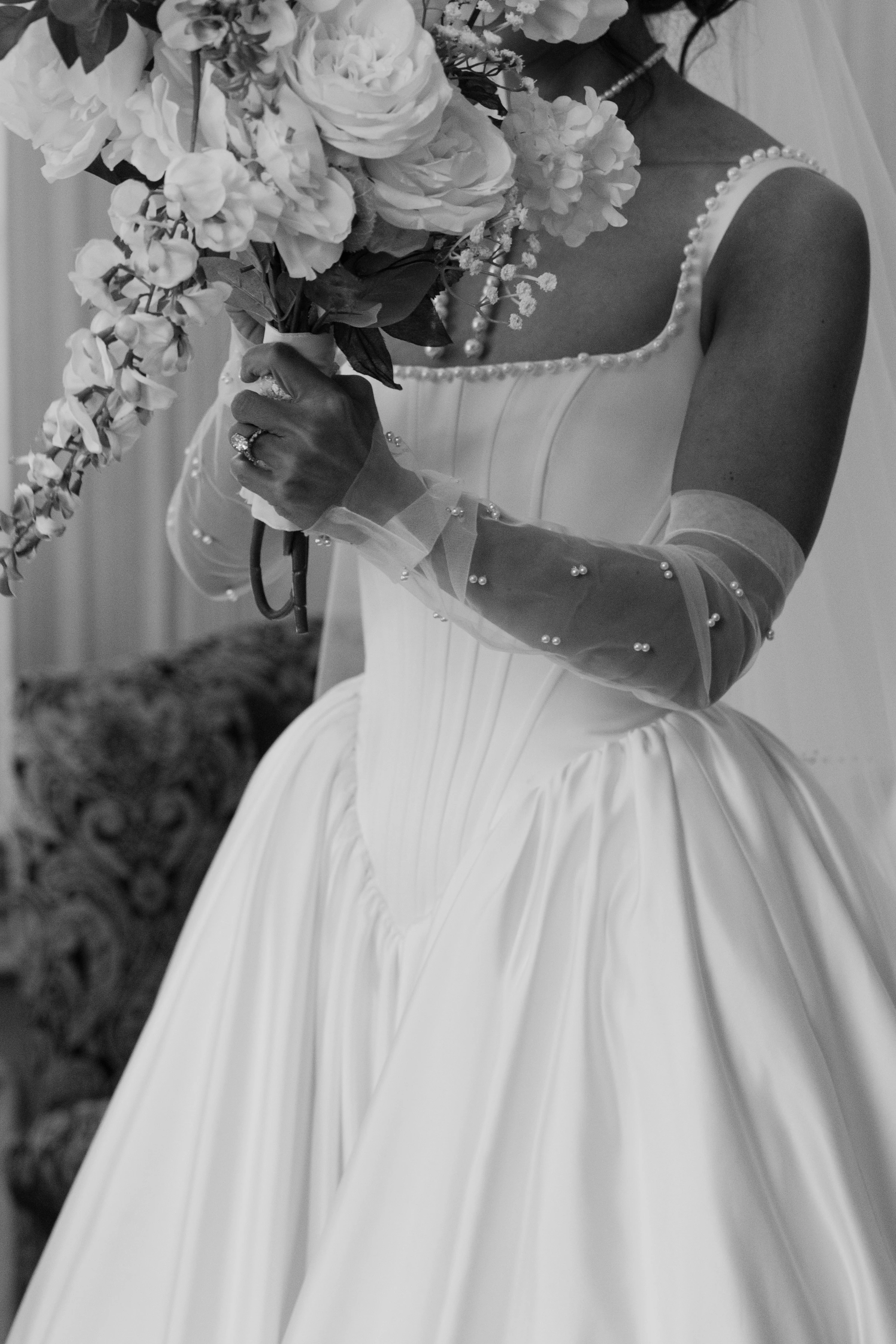 Tasia's corseted gown and pearl tulle gloves as she holds her bouquet, black and white