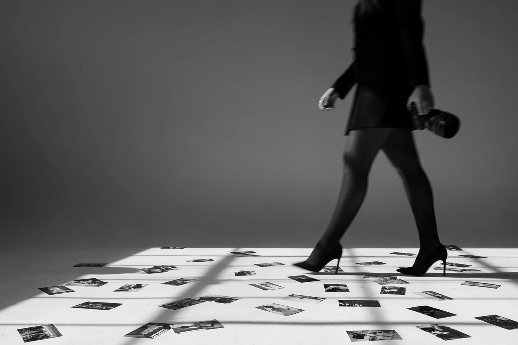 Tiana walking across a studio floor scattered with wedding prints, camera in hand